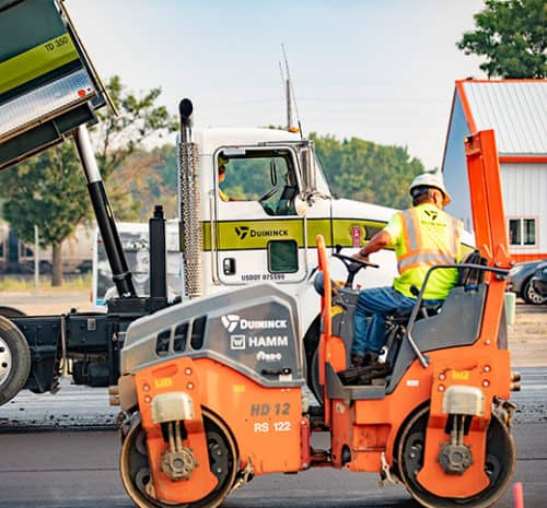 Orange HAMM Tandem roller in front of truck on construction site.