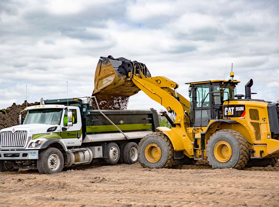 CAT 950M loader dumping dirt into a tandem truck.