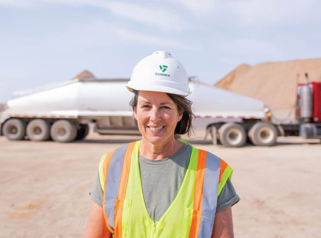 Woman truck driver smiling in front of live bottom semi-truck