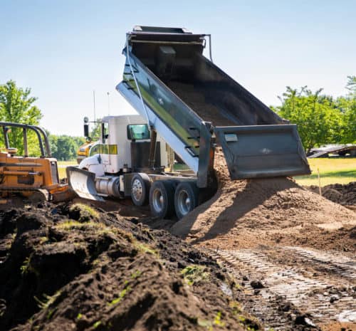 Tandem truck dumps dirt at the site of a grading project.