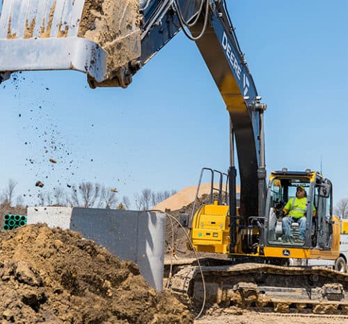 Man in excavator dropping dirt overtop underground utilities.