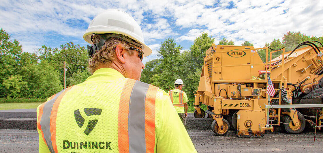 A construction worker in a safety vest and hard hat, with Duininck on the back