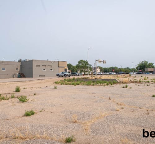 Before photo of parking lot with weeds and gravel with building in the background.