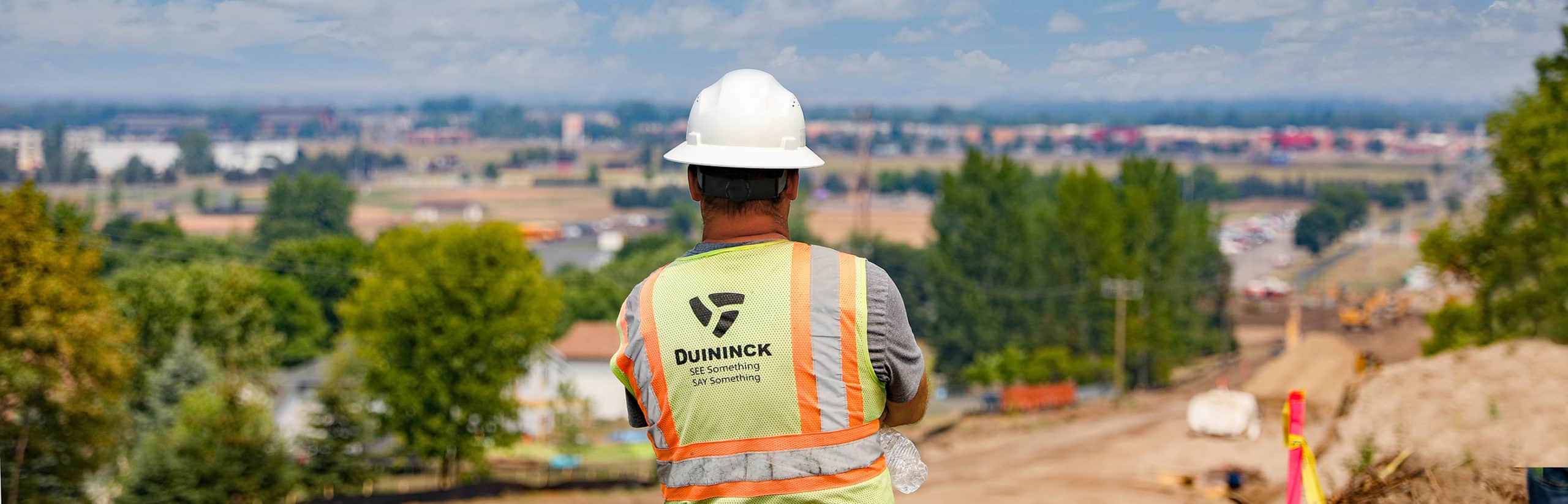 Man in Duininck safety vest and hard hat overlooking a construction site on a hill.
