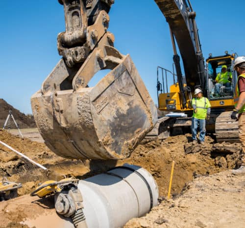 Crew lead directing excavator operator where to dump dirt overtop underground utilities.
