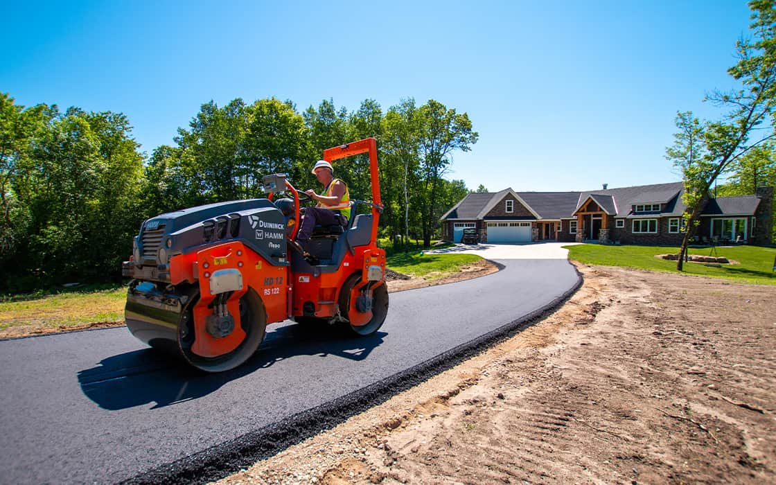 Man driving a tandem roller over a new residential asphalt driveway.