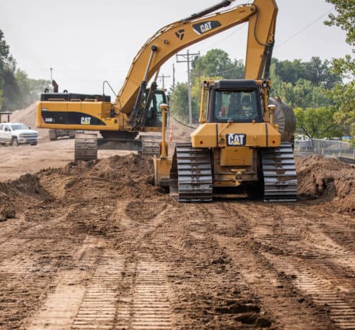 Dozer and excavator grading on highway road.