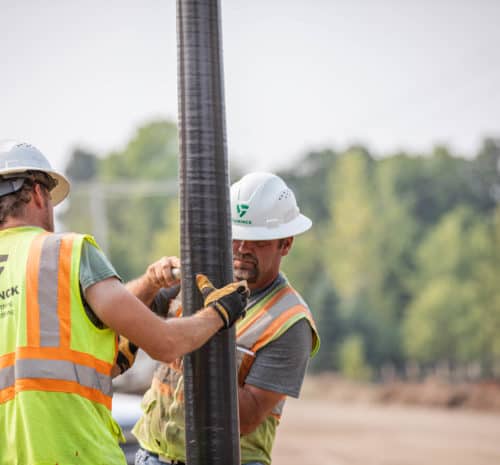 Two men in safety vests and hard hats working on electrical on jobsite.