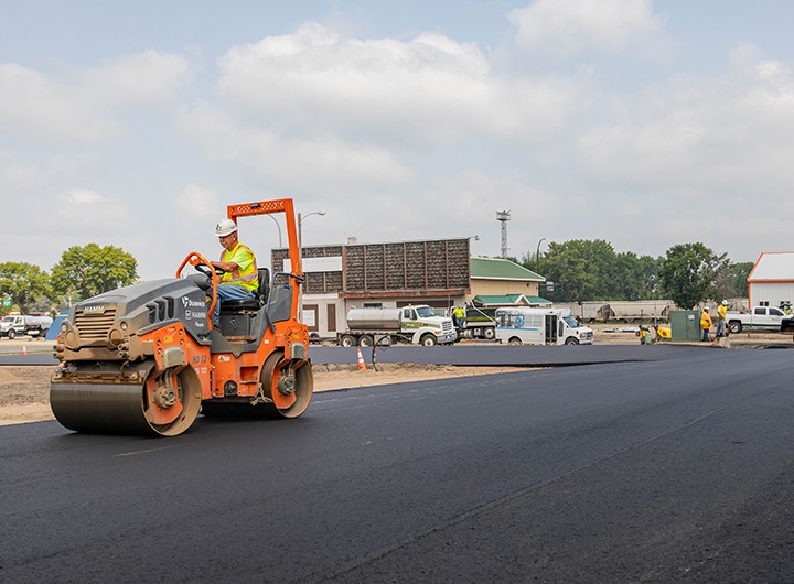 Man driving tandem roller over new asphalt commercial parking lot.