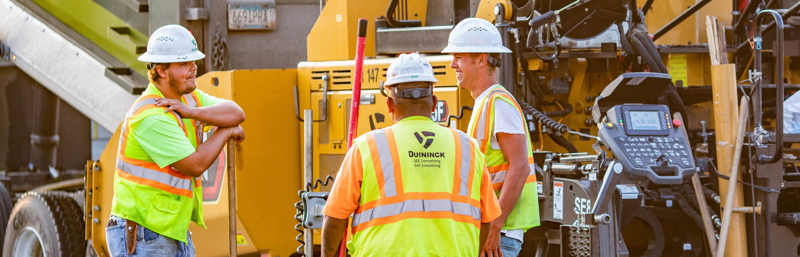 Three construction men smiling and talking on a commercial paving project.