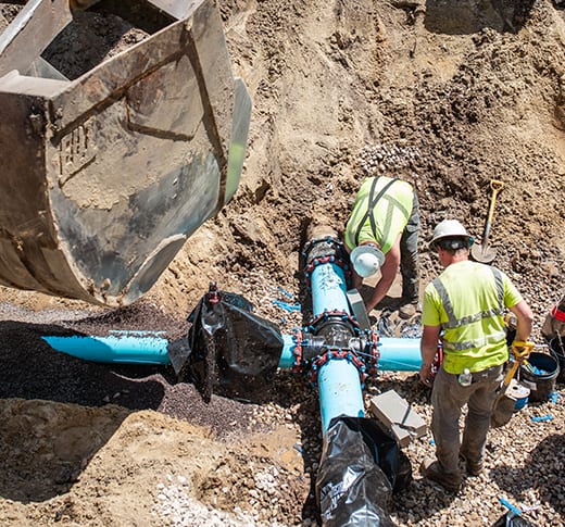 Two men installing a water main in a trench.