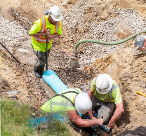 Two men install a water main while one man assists.