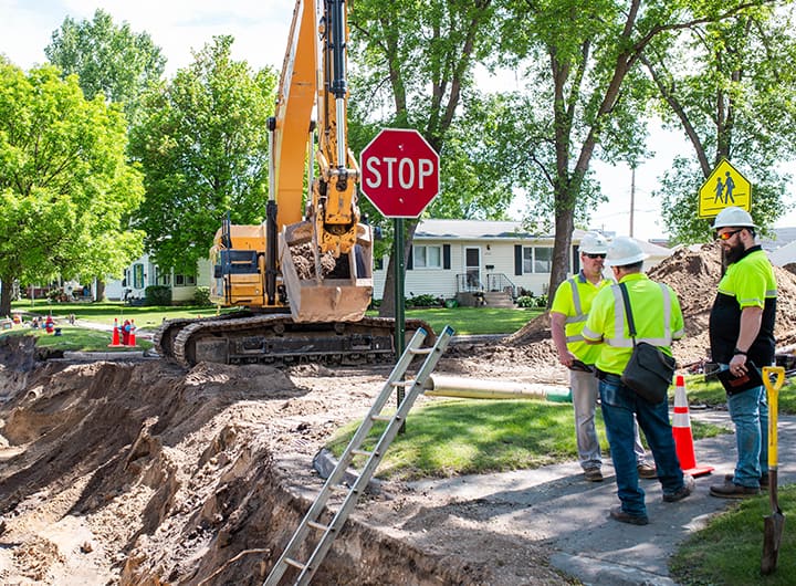 Three men in safety vests and hard hats talking in front of an underground construction site.