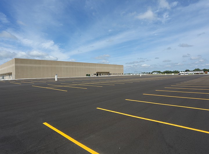 New asphalt parking lot with parking spots and large FedEx distribution center in the background.