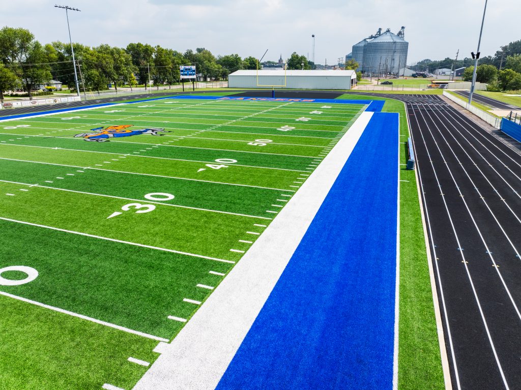 Aerial view of vibrant football field with track and community backdrop