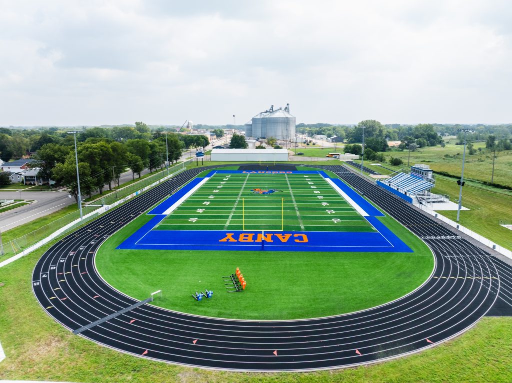 Aerial view of a vibrant green football field with blue track surrounding it.