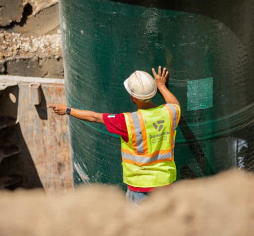 Guides a large green pipe into place at a construction site.