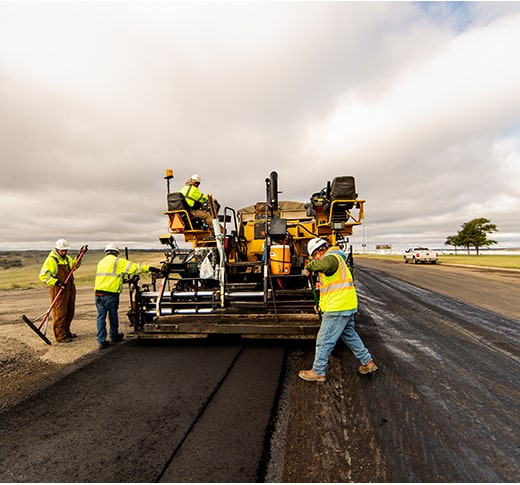 Construction workers in high-visibility clothing operate heavy paving equipment - Pierre Paving