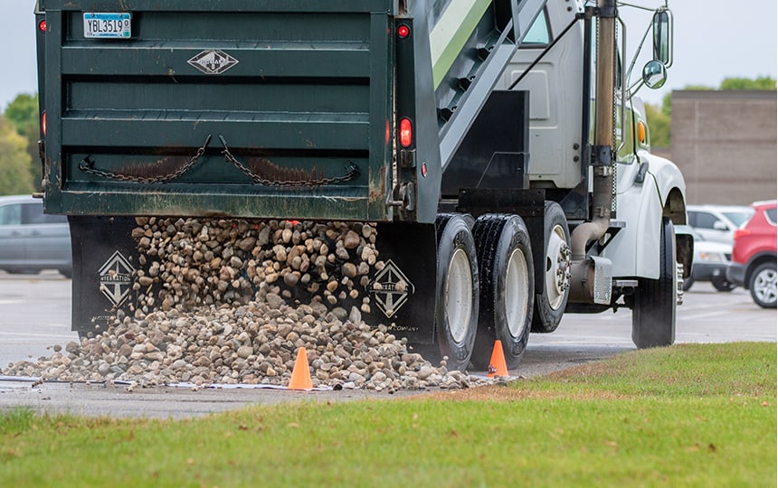 A dump truck unloads a pile of rocks onto a paved surface - Roosevelt Rocks