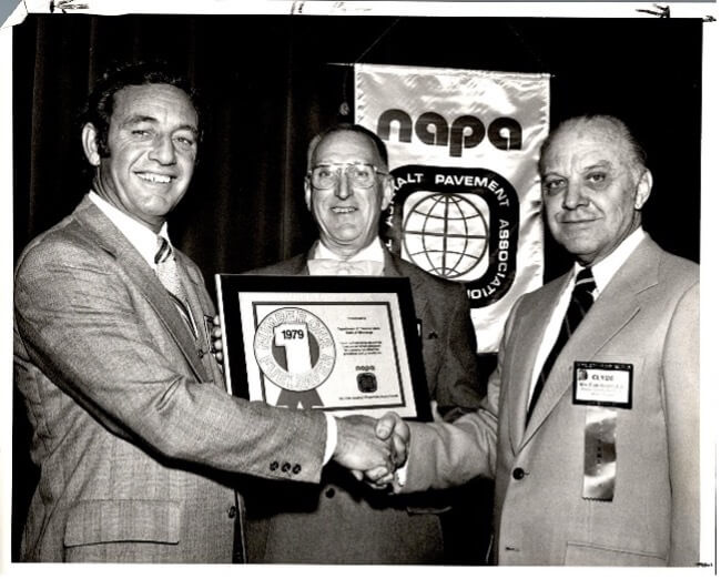 Three men in suits at an award ceremony with a NAPA banner.